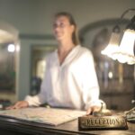 A concierge stands at a hotel reception desk under ambient lighting, ready to assist guests.